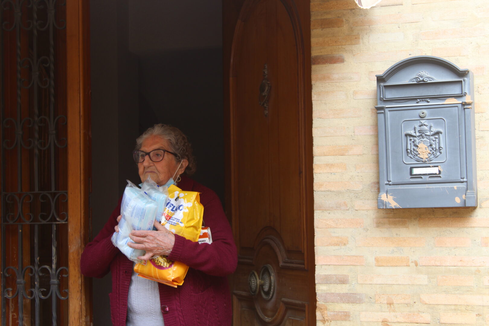 Carmela recoge la ayuda que le proporcionan los voluntarios desde la puerta de su casa